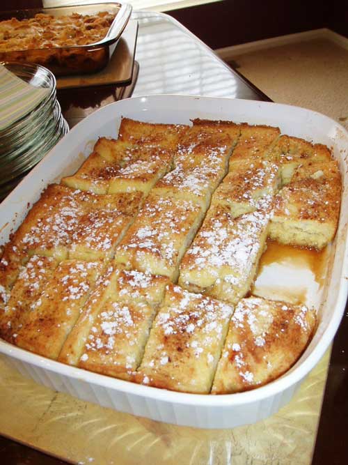 A finished French Toast Bake in a white baking dish. It has been cut into rectangles, and one of the pieces is missing.