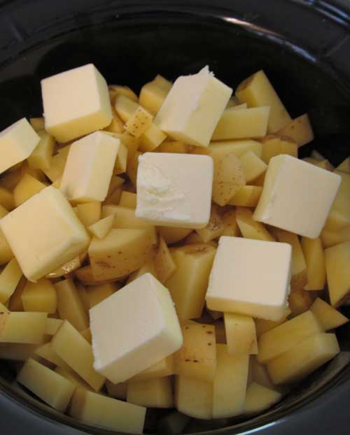 Potatoes cut into chunks, and covered with pats of butter. Everything is in a black slow cooker pot.