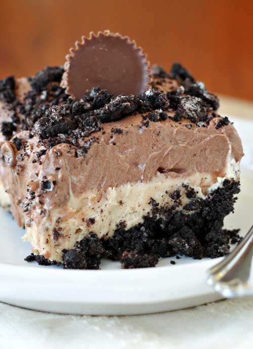 A slice of Chocolate Peanut Butter No-Bake Dessert sits on a white plate. A peanut butter cup is resting on top as a garnish.