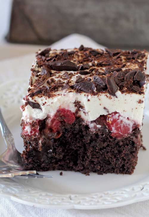 This Black Forest Poke Cake is a gooey chocolate cake filled with hot fudge and cherry pie filling. It's topped with fresh whipped cream and chocolate shavings.