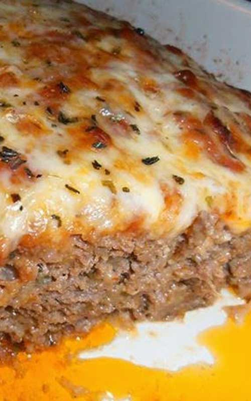 Diagonal view of a finished Italian Meatloaf covered in cheese. The end piece is removed to show the texture.