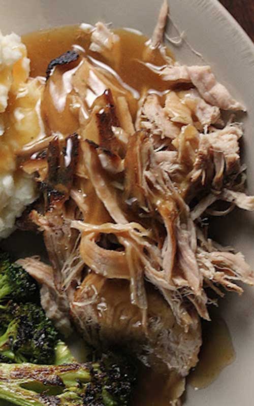 Shredded Trisha Yearwood's Crock Pot Pork Loin covered with gravy, on a white plate.