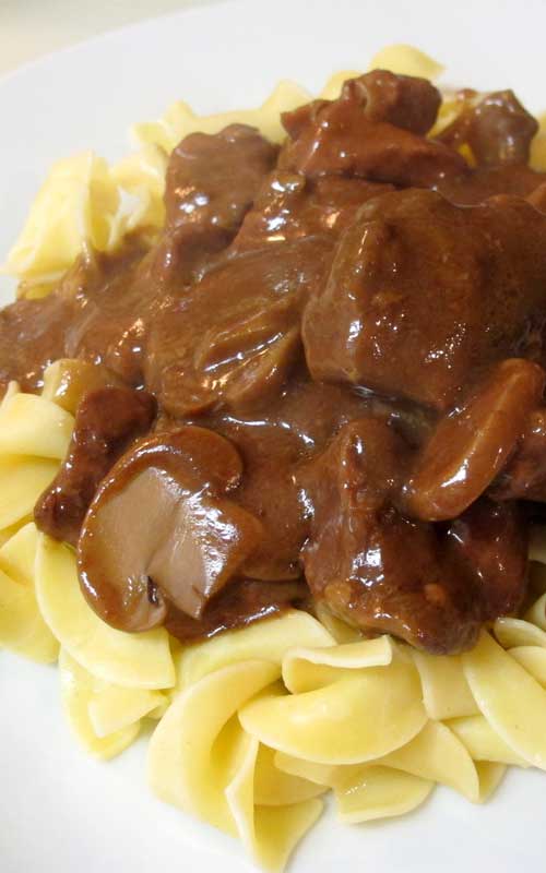 Crockpot Beef Tips & Gravy served over egg noodles, on a white plate.