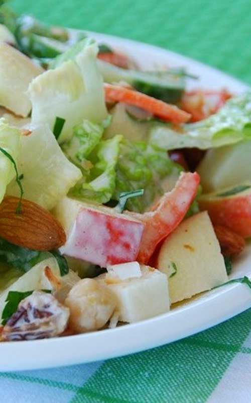Lettuce, tomato, apple, and jicama in a white bowl. The salad is lightly covered in a white salad dressing.